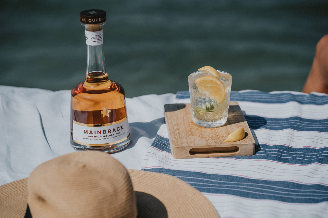 Bottle of Mainbrace Premium Golden Rum next to glass and hat